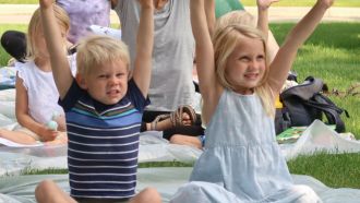 Two children sitting outside with arms in the air