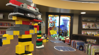Small lego buildings on top of a bookshelf in the library