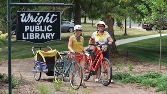 two bike riders walking bikes by WrightLibrary sign